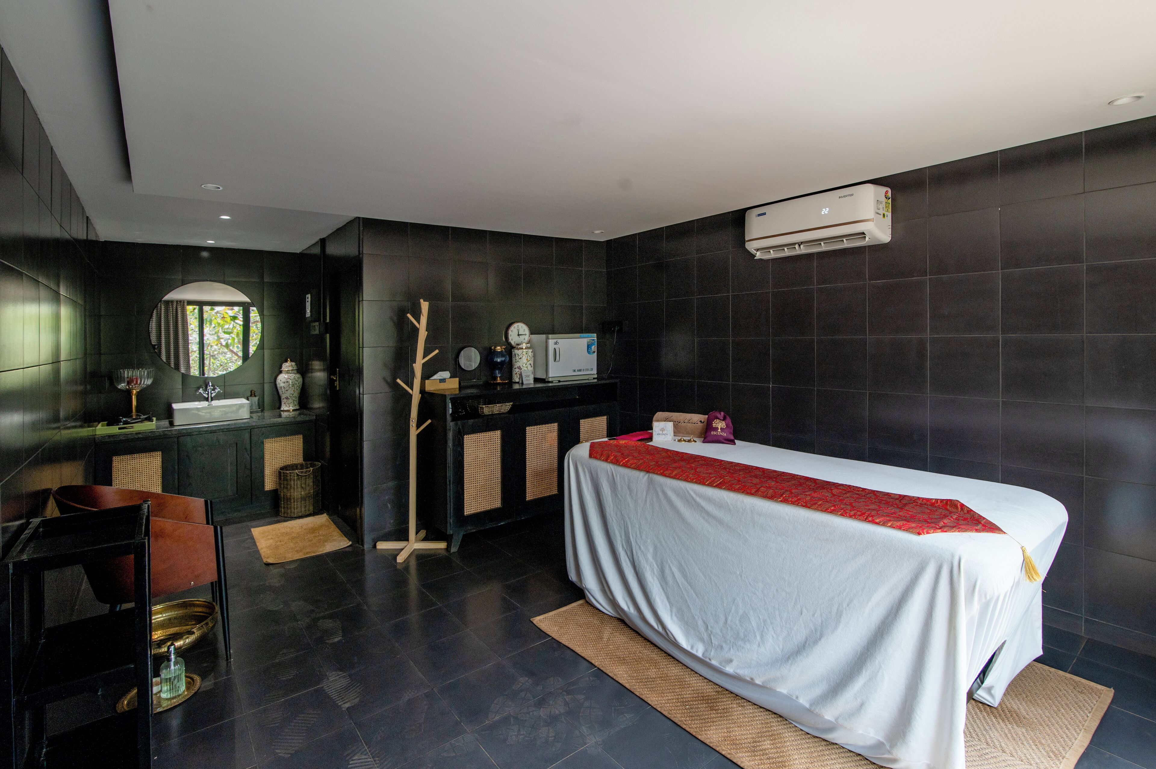 Una habitación de hotel moderna con una cama, un escritorio, un espejo redondo, un ventanal pequeño y un aire acondicionado de pared.