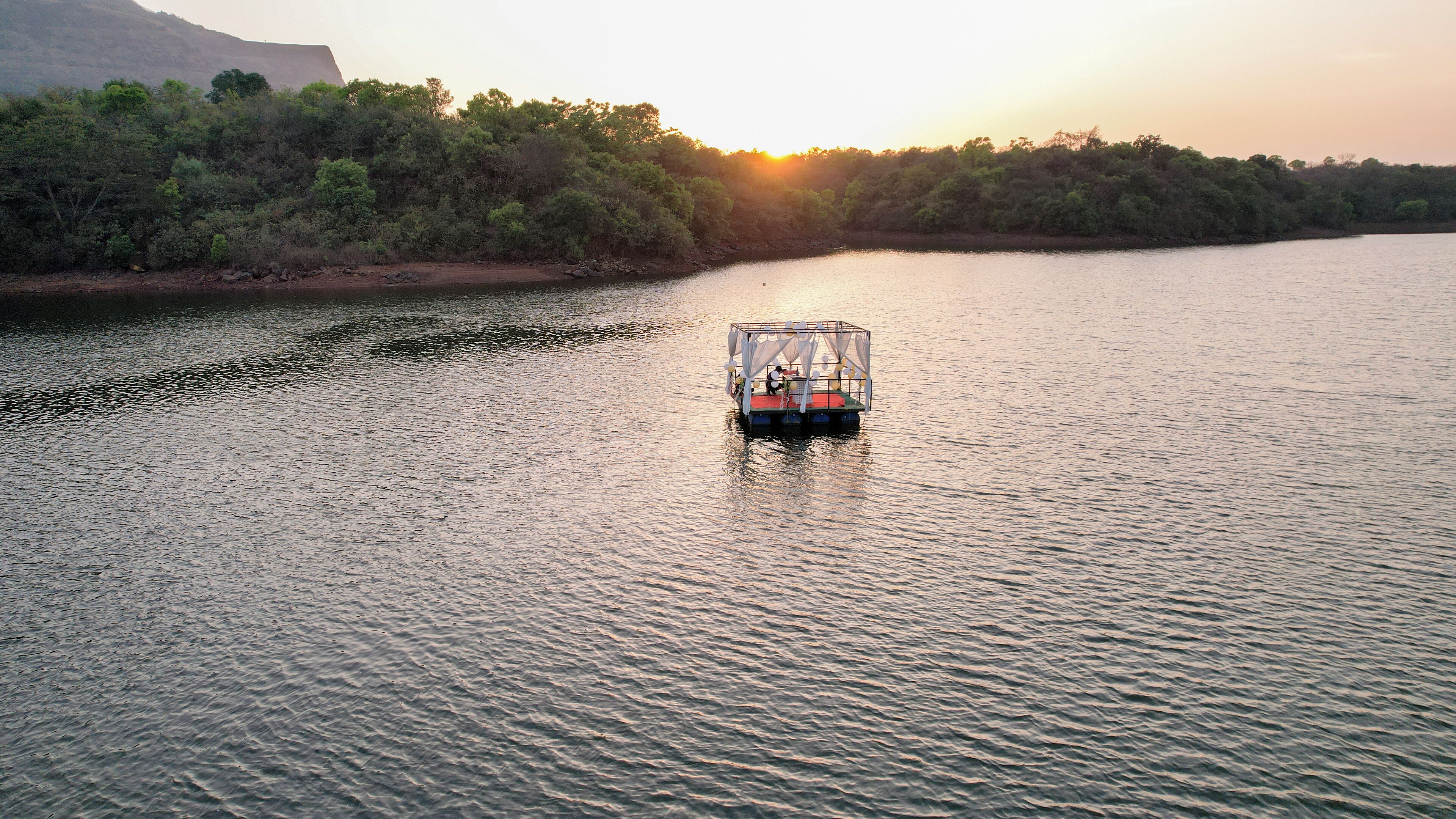 A boat on a calm river with a forested bank and a mountain in the background.