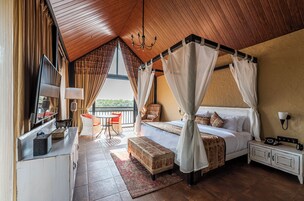 A bedroom with a canopy bed, a desk with a lamp, a chair, a small table, and a nightstand with a phone.