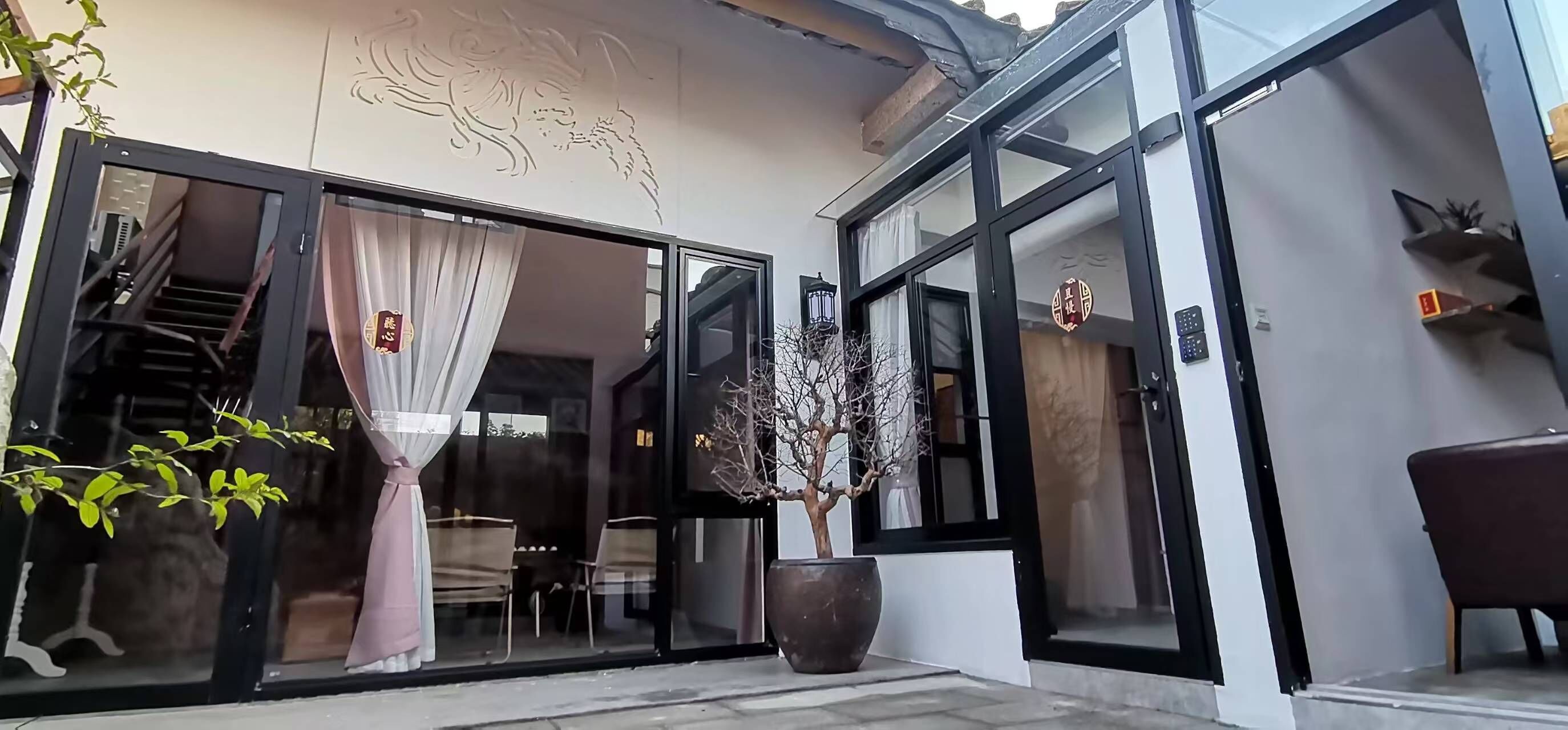 A modern building with large glass doors, a staircase inside, and a potted tree outside.