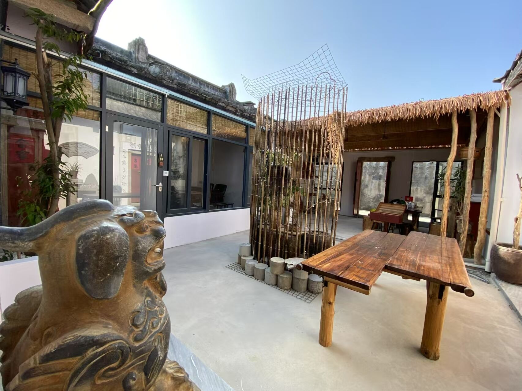 Un edificio moderno con grandes ventanales, una valla de bambú y una mesa de madera en el patio.