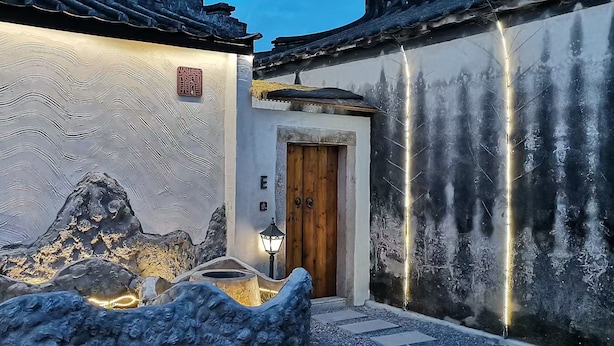 A traditional building with a wooden door, a stone wall with a wavy pattern, and a small garden with rocks and lights. - Serenity Courtyard Hotel (Shantou)