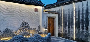 A traditional building with a wooden door, a stone wall with a wavy pattern, and a small garden with rocks and lights. - Serenity Courtyard Hotel (Shantou)