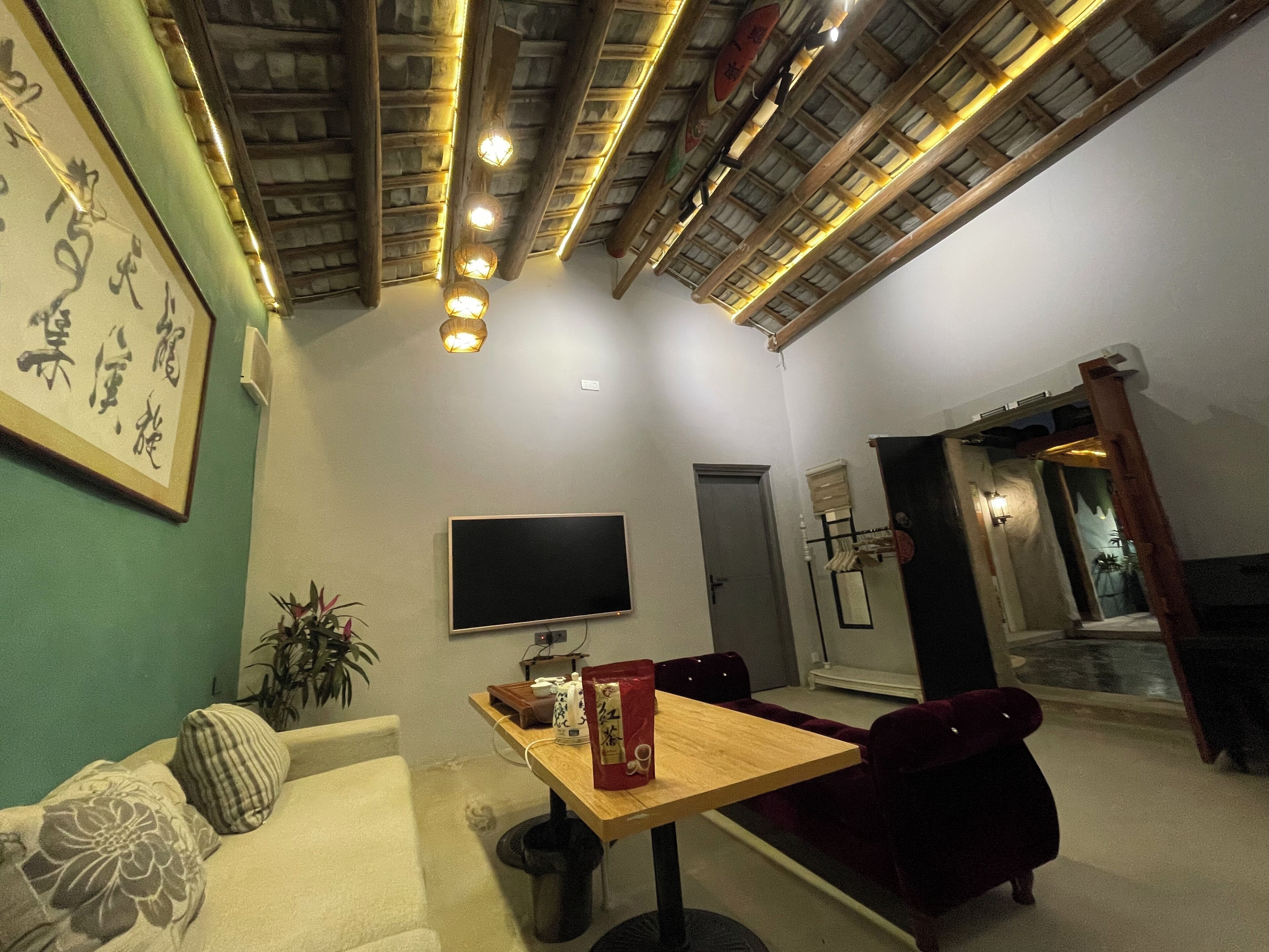 A living room with a sofa, a dining table, a TV, and a ceiling with exposed beams and lights.