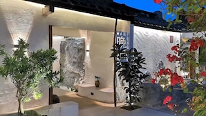 A modern building with a stone facade, a large glass door, and a small garden area with potted plants and red flowers. - Serenity Courtyard Hotel (Shantou)