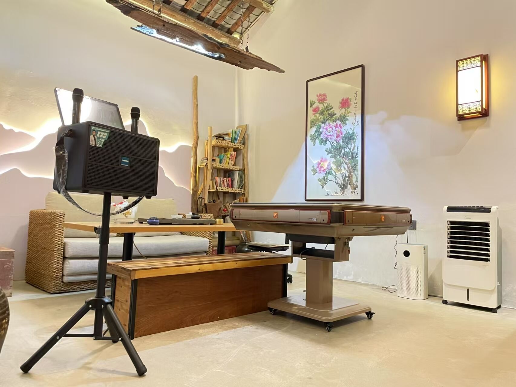 Una habitación con una mesa de masajes, una silla de masaje, una estantería, una obra de arte enmarcada y una lámpara fijada a la pared.
