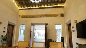 A spacious room with a high ceiling, wooden beams, and a central light fixture. There are two windows and a door leading outside. - Serenity Courtyard Hotel (Shantou)