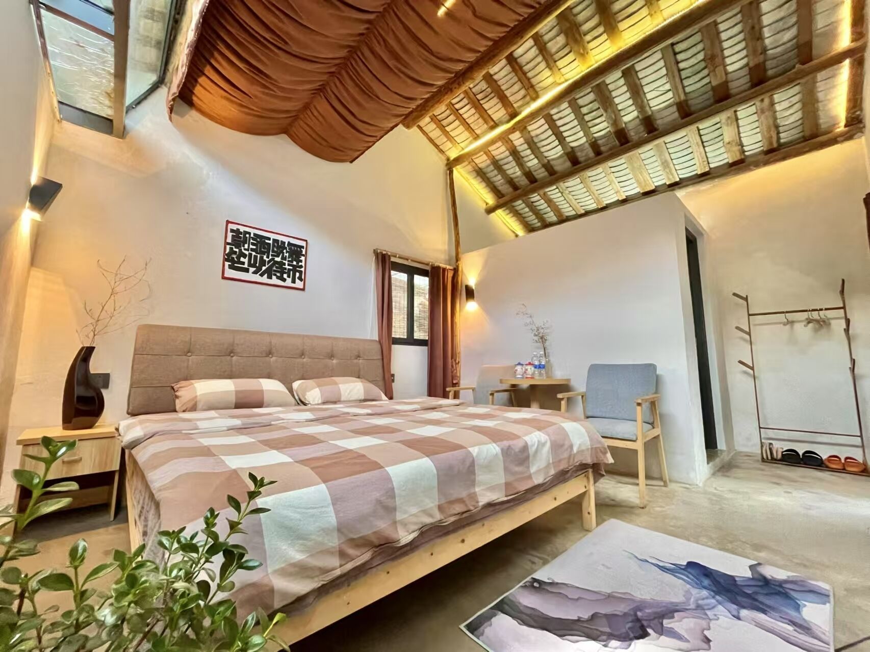 Un dormitorio con una cama grande, un cabecero de madera, una mesita con un jarrón y un zapatero.