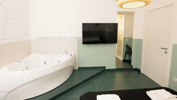 A modern bathroom with a freestanding bathtub, a flat-screen TV mounted on the wall, and a staircase leading to another room. - O Effe Games Vatican (Rome)