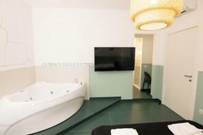 A modern bathroom with a freestanding bathtub, a flat-screen TV mounted on the wall, and a staircase leading to another room. - O Effe Games Vatican (Rome)