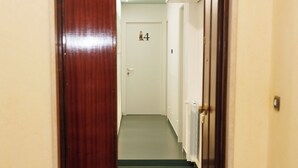 A hallway with a wooden door on the left and a white door with the number 4 on the right. A black mat with colorful text is on the floor. - O Effe Games Vatican (Rome)