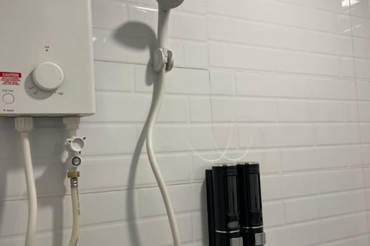 A shower control panel with a caution label, a white hose, and a black object on the wall.