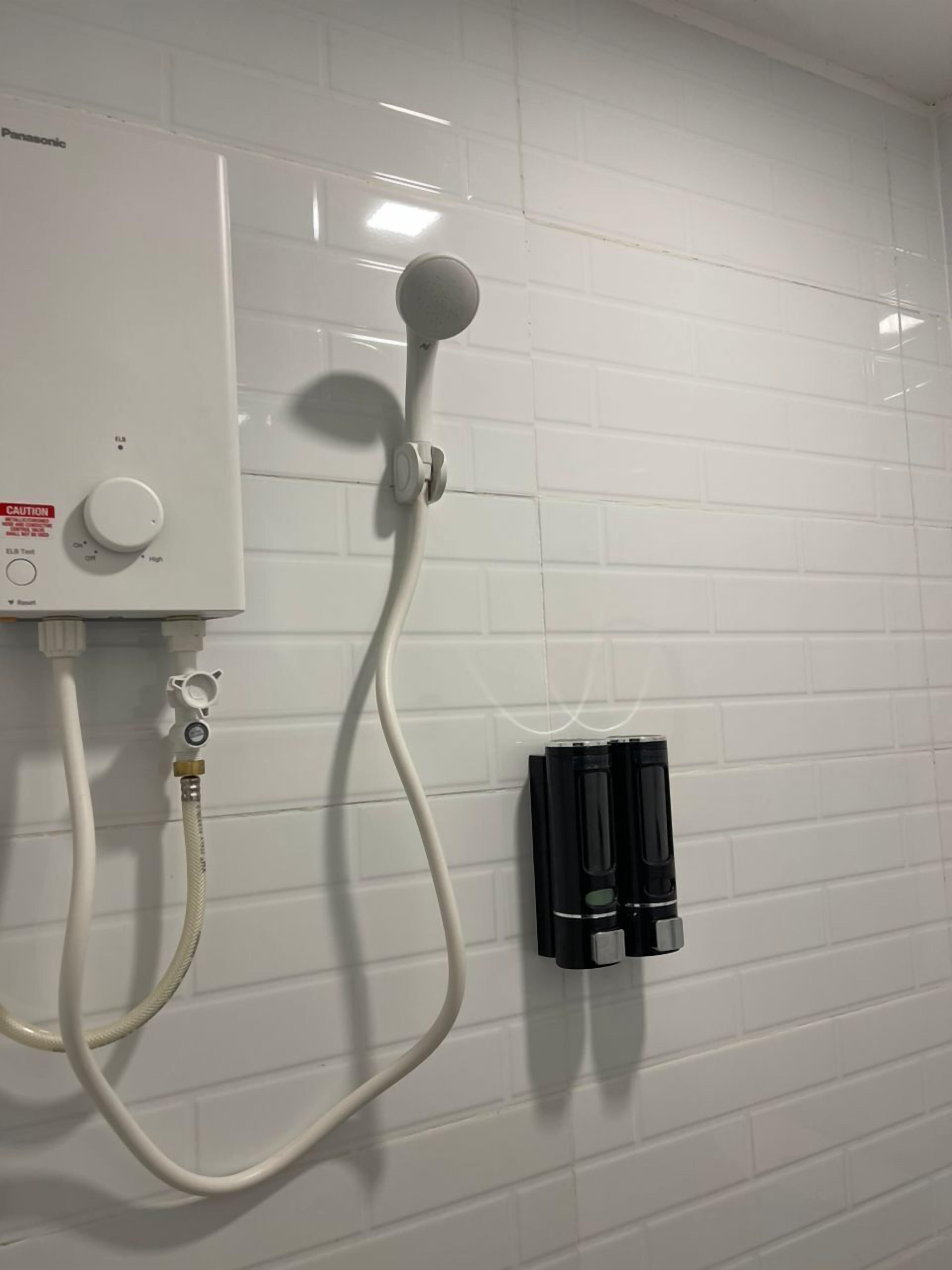 A white tiled wall with a white water heater, a control knob, and a black electrical outlet box.
