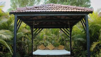 A covered wooden structure with a swing bed, surrounded by lush greenery.