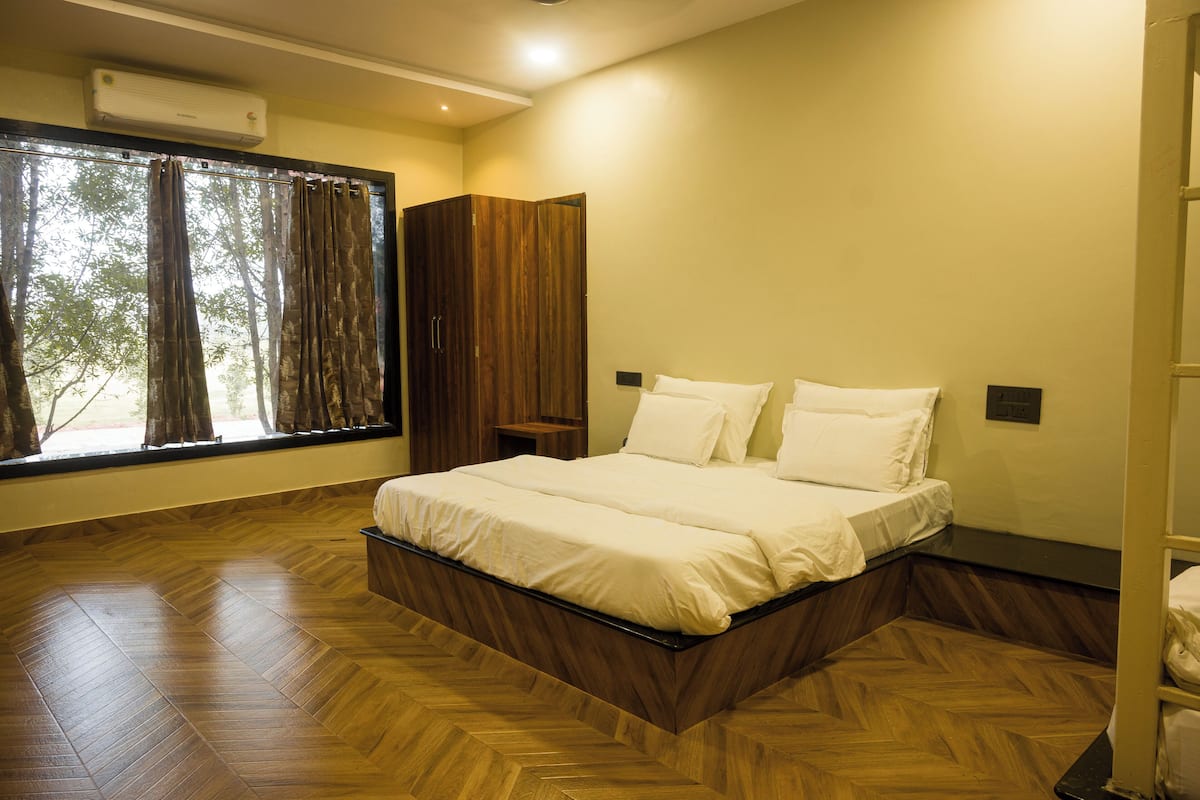 A bedroom with a wooden floor, a bed, a window with curtains, and a wardrobe.