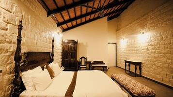 A bedroom with a large bed, wooden headboard, a bench, a wooden cabinet, and stone walls.