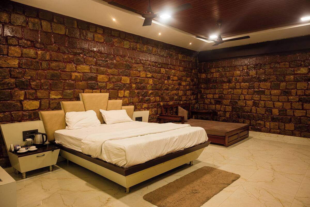 A bedroom with a stone wall, a bed, a nightstand, a coffee maker, and a seating area.