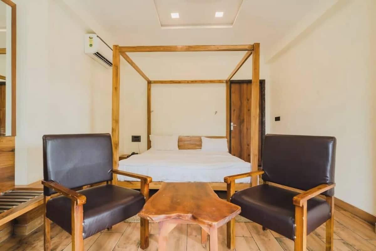 A room with a four-poster bed, two leather chairs, a wooden coffee table, and a small table with a cloth.