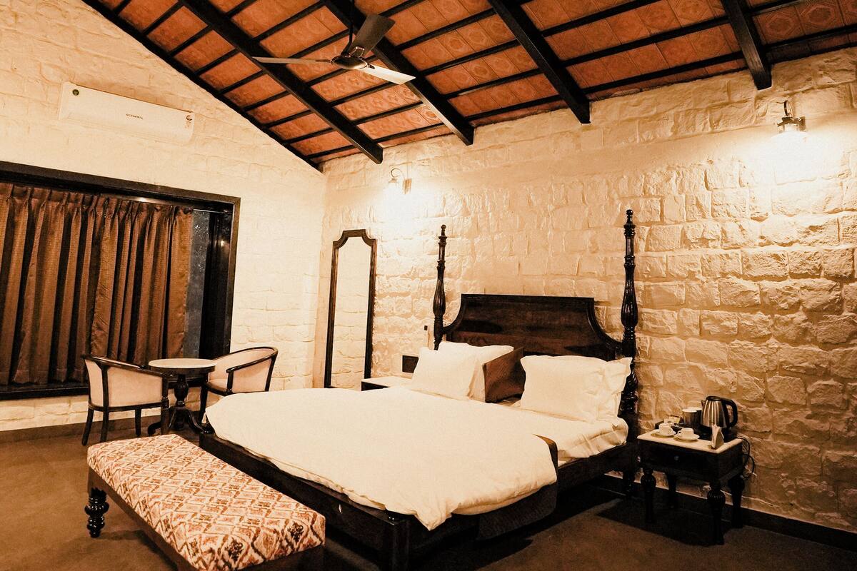 A bedroom with a large bed, a bench, a table, and a mirror.