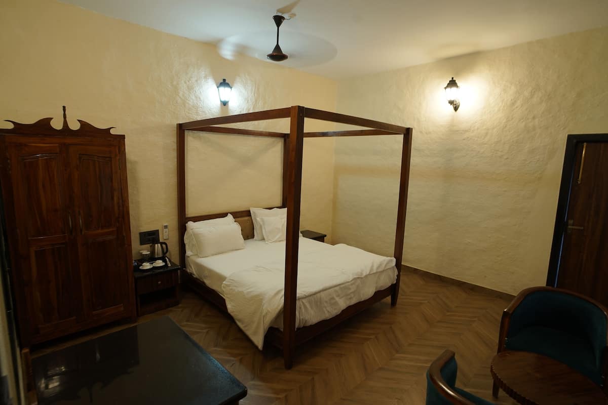 A four-poster bed with a wooden frame, a wooden wardrobe, a desk, and a chair in a room with wooden flooring.