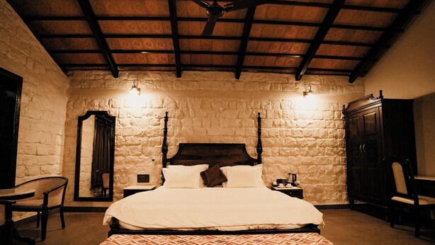 Un dormitorio con una cama con dosel, paredes de piedra, techo de madera y colcha estampada.
