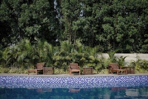 A pool area with tiled edges, wooden lounge chairs, and lush greenery in the background. - AKAY Resort & Villas (Rajnandgaon)