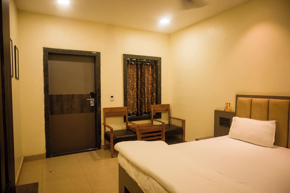 A hotel room with a bed, two wooden chairs, a small table, a nightstand, a mirror, and a door.