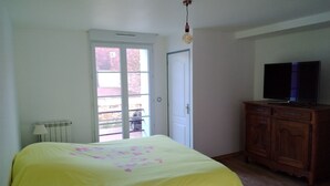 Ein Schlafzimmer mit einem Bett, einem Fernseher, einem Holzschrank und einer Tür zu einem Außenbereich.