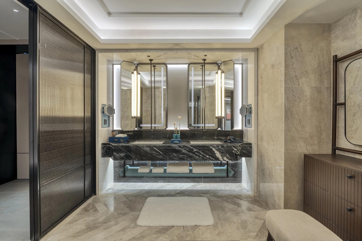 Un baño moderno con un espejo grande, lavamanos doble y un banco.