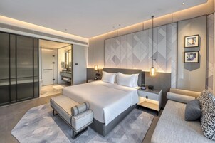 Una habitación de hotel moderna con una cama grande, un sofá, un escritorio y un vestidor.
