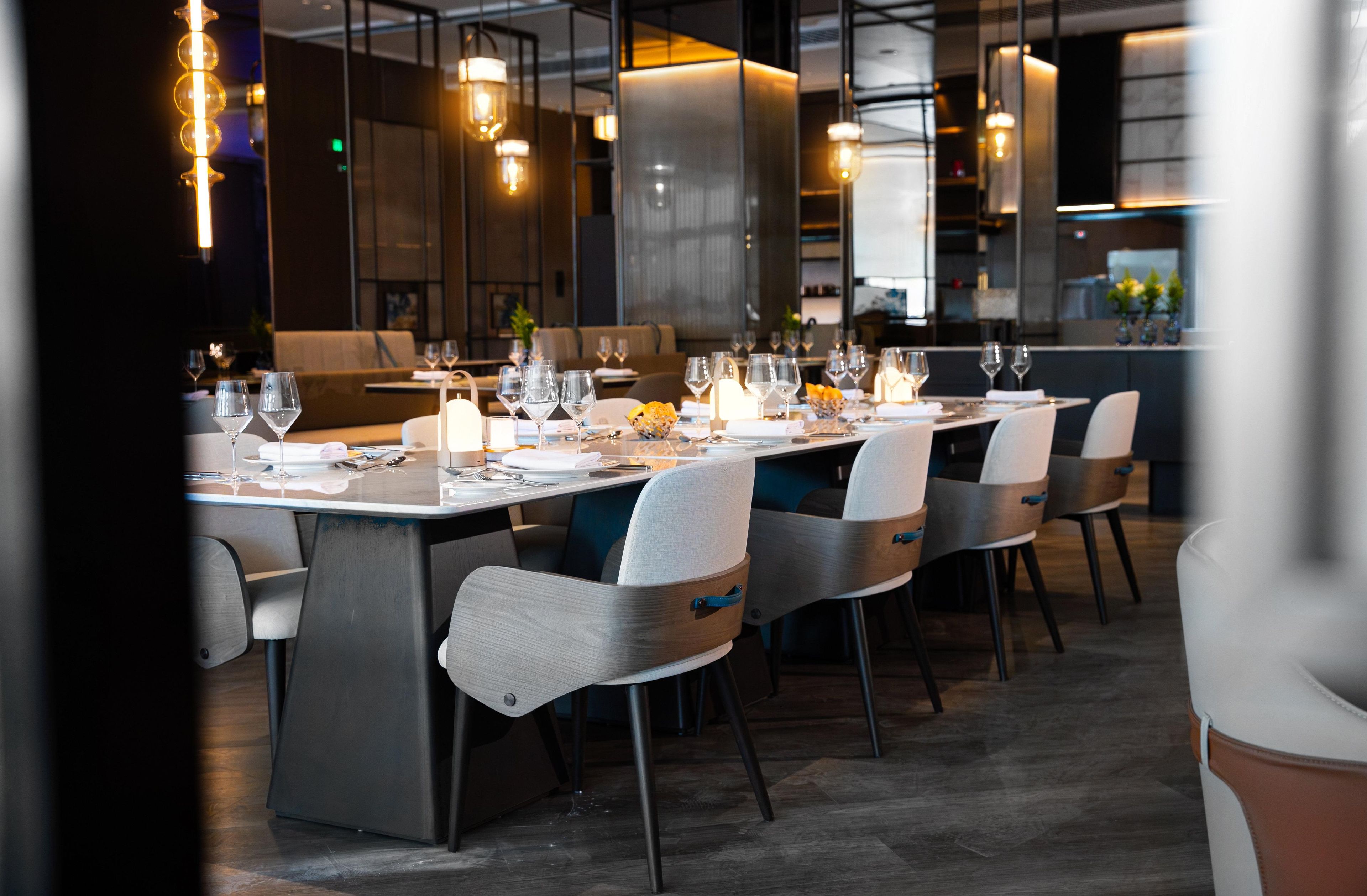 Un restaurant moderne avec une longue table à manger dressée pour le repas, entourée de chaises.