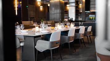 Een modern restaurant met een lange eettafel, gedekt voor een maaltijd, omringd door stoelen.