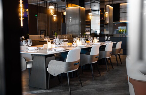 A modern restaurant with a long dining table set for a meal, surrounded by chairs.