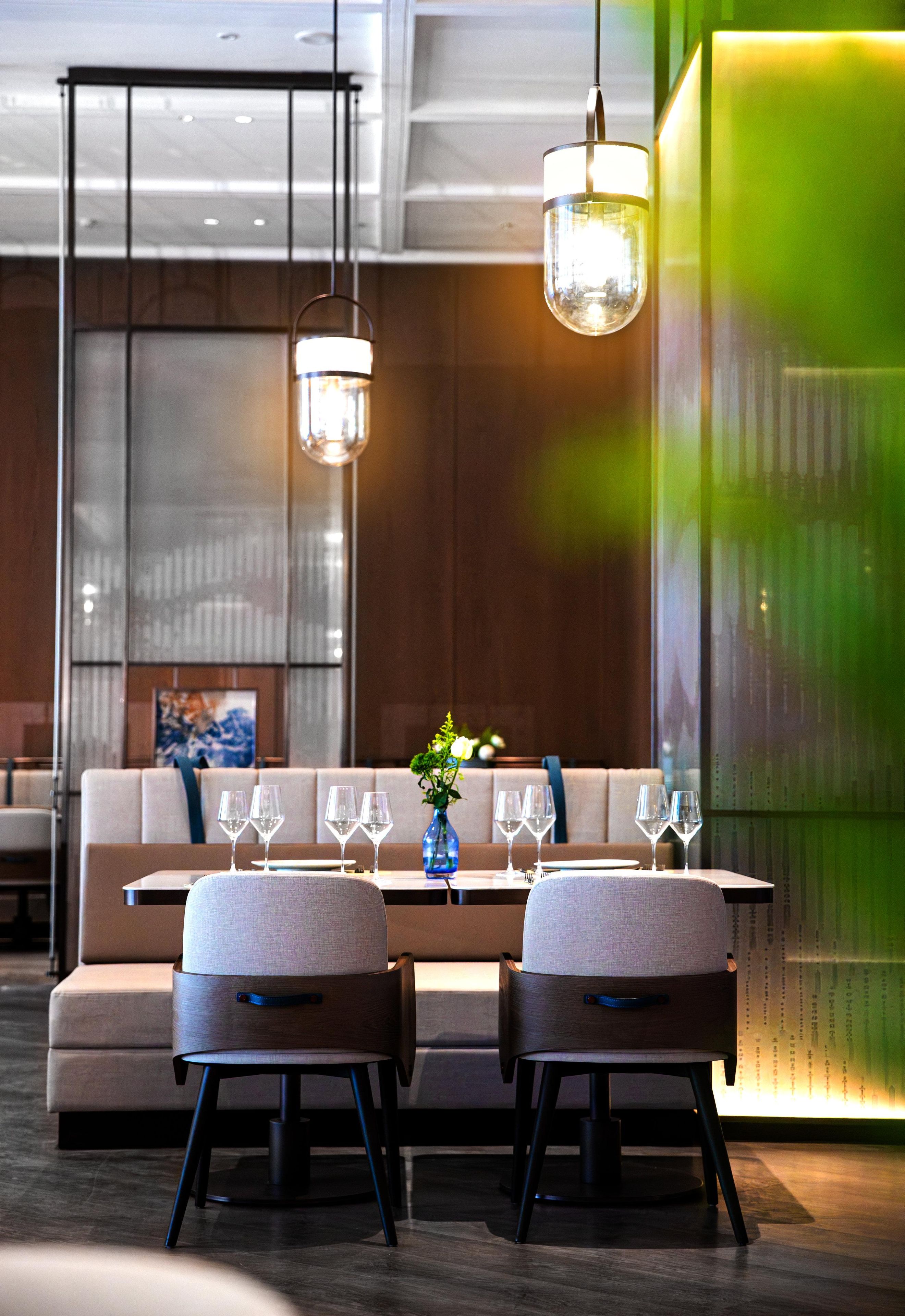 A modern dining area with a table set for four, two chairs, and a vase of flowers.