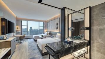 A modern hotel room with a large bed, a desk, a sitting area, a large mirror, and a bathroom with a marble countertop.