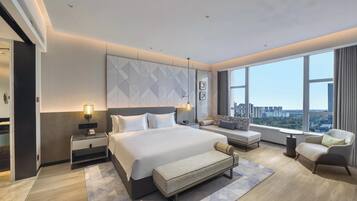 Een moderne hotelkamer met een groot bed, een zithoek en uitzicht op de stad, met een stadsbeeld zichtbaar door het raam.