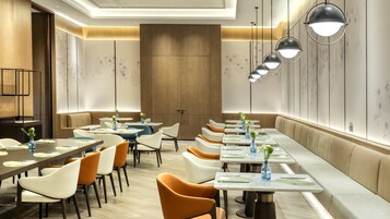 Un comedor moderno con mesas largas, asientos acolchados e iluminación colgante.