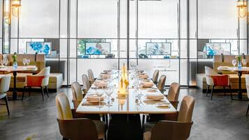 Un comedor moderno con una larga mesa dispuesta para una comida, ventanas amplias y obras de arte en las paredes.