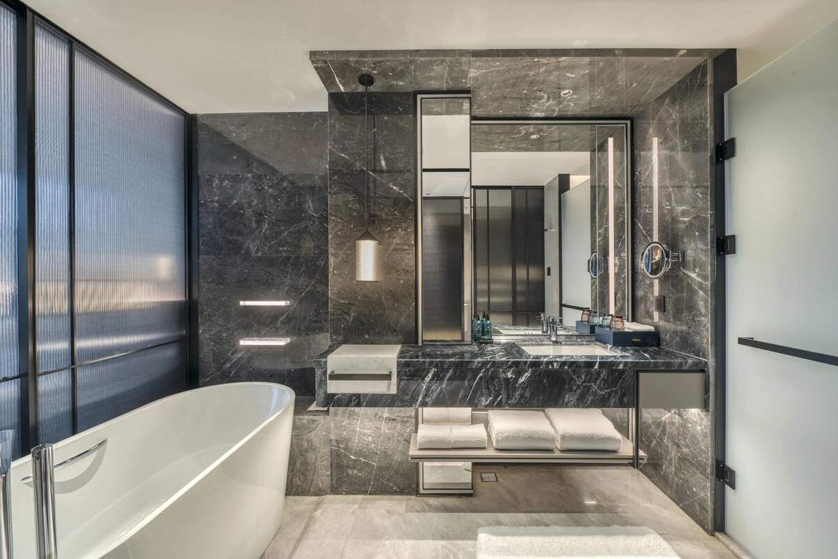 A modern bathroom with a freestanding bathtub, a large mirror, and a marble countertop.