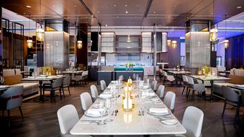 A modern restaurant with a long dining table set for a meal, surrounded by chairs.