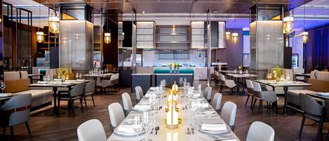 A modern restaurant with a long dining table set for a meal, surrounded by chairs.