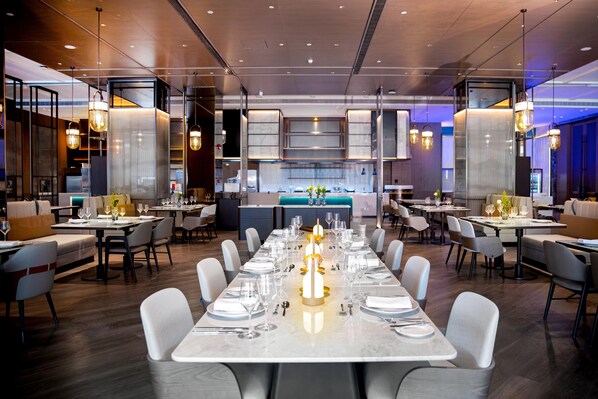 A modern restaurant with a long dining table set for a meal, surrounded by chairs.