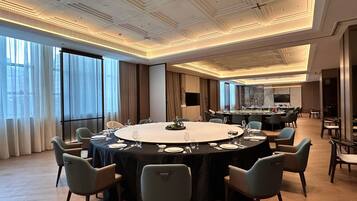 A conference room with a large oval table, surrounded by chairs, in a modern hotel setting with large windows and a high ceiling.
