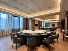 A conference room with a large oval table, surrounded by chairs, in a modern hotel setting with large windows and a high ceiling.