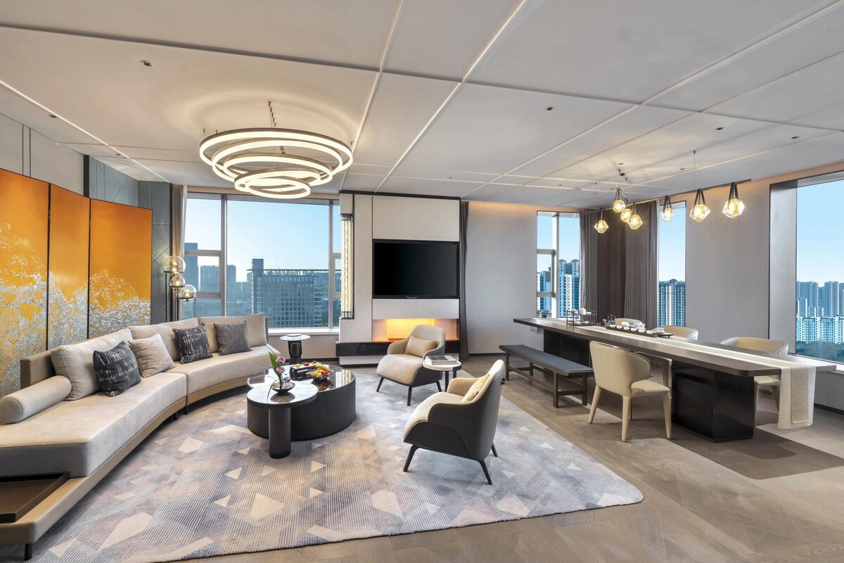 Un salon moderne avec un canapé aux lignes courbes, une table basse et un coin repas comprenant une longue table et des chaises.