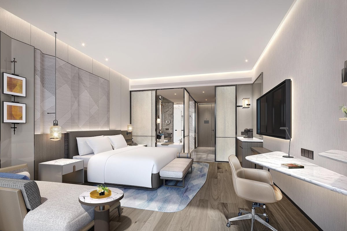 A modern hotel room with a large bed, a desk, a chair, and a TV.