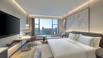 A modern hotel room with a large bed, a flat-screen TV, a desk, and a large window offering a city view.