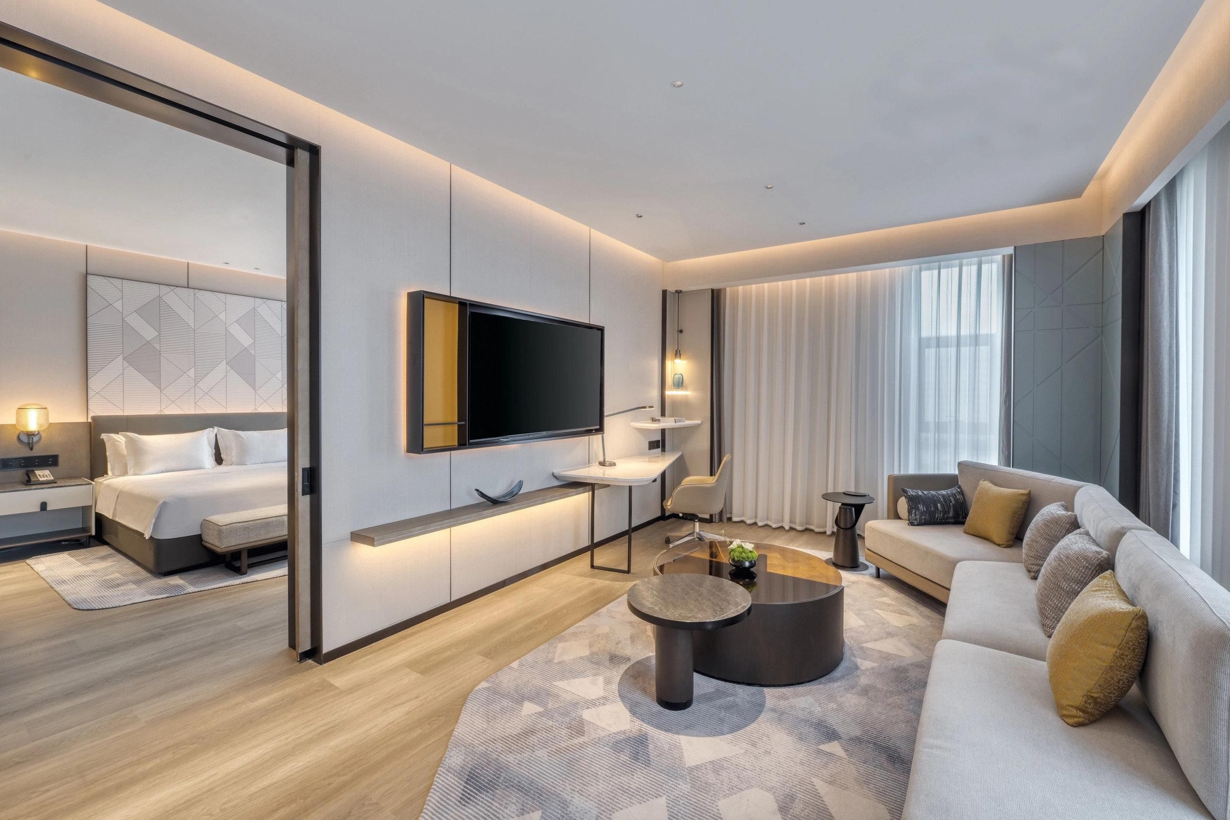 Een moderne hotelkamer met een bed, een bank, een salontafel, een televisie en een bureau.