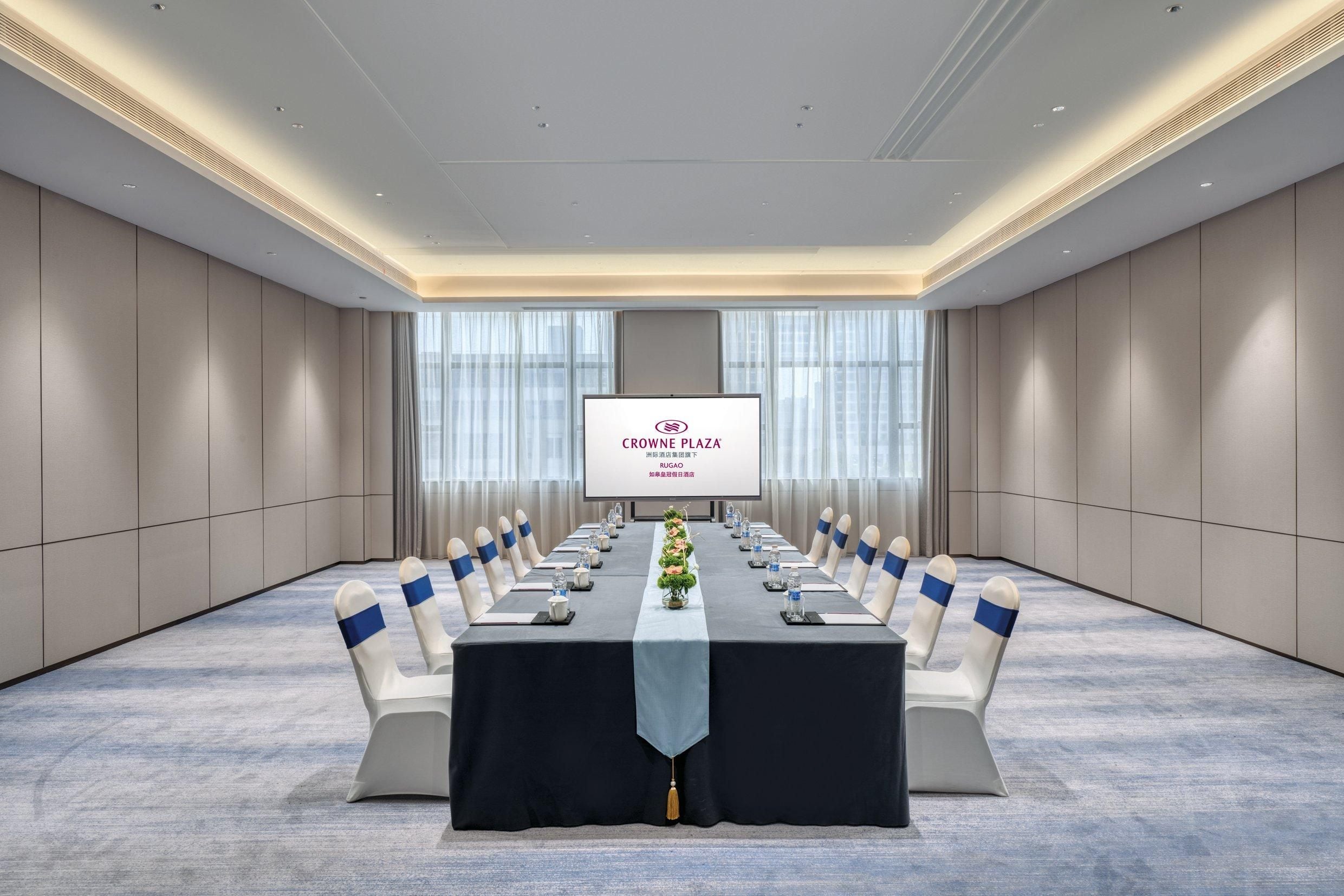 A conference room with a long table, chairs, and a screen displaying "CROWNE PLAZA".
