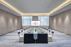 Un salón de conferencias con una larga mesa, sillas y una pantalla que muestra 'CROWNE PLAZA'.